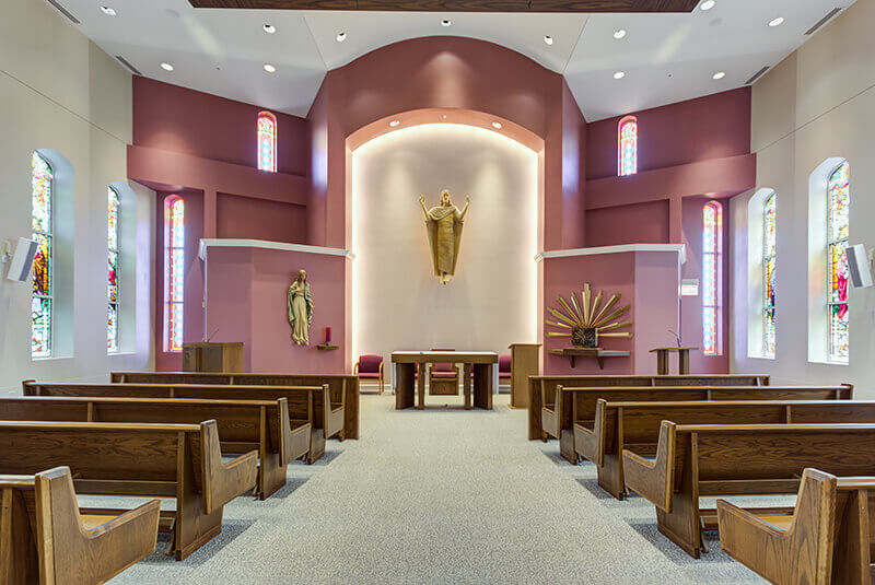 Chapel interior featuring altar, religious statues, and stained-glass windows at Amazing Grace Senior Living