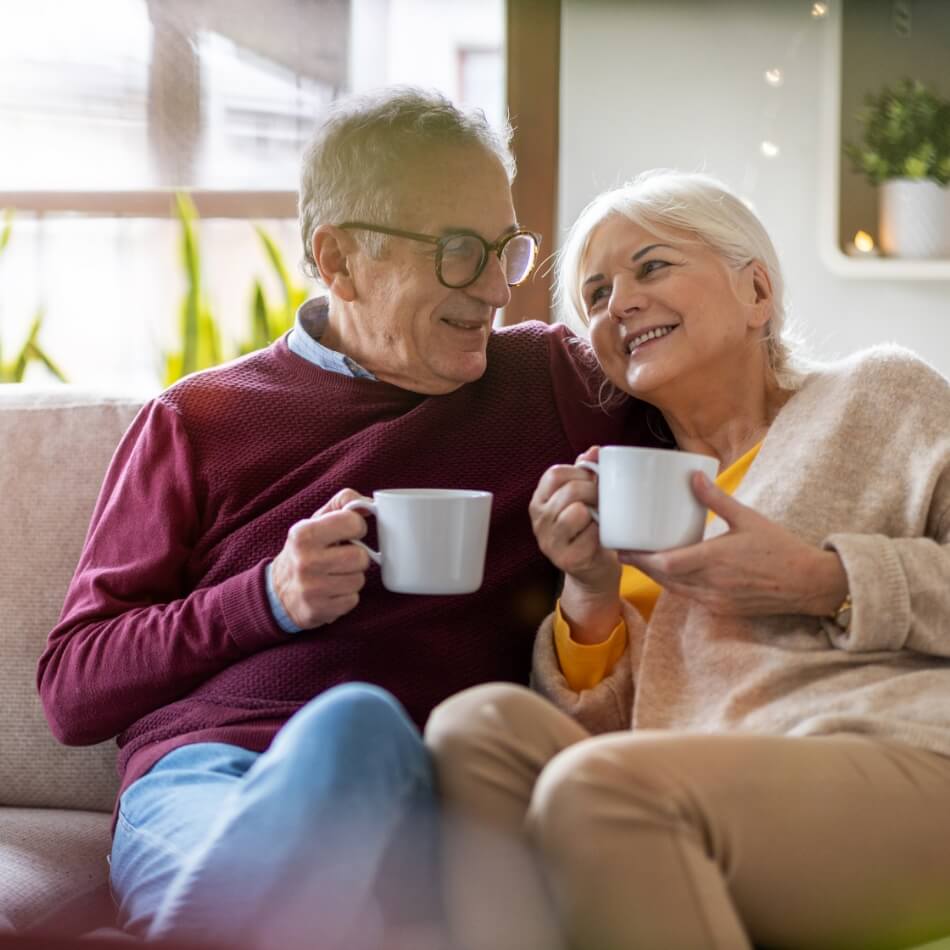 Senior couple smiling and sharing coffee together in a comfortable living space at Amazing Grace Senior Living
