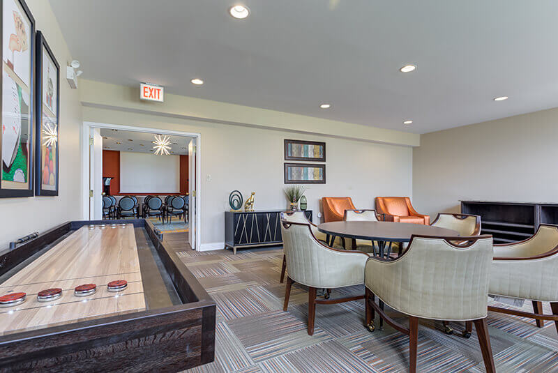 Game room with shuffleboard table, lounge seating, and modern decor at Amazing Grace Senior Living